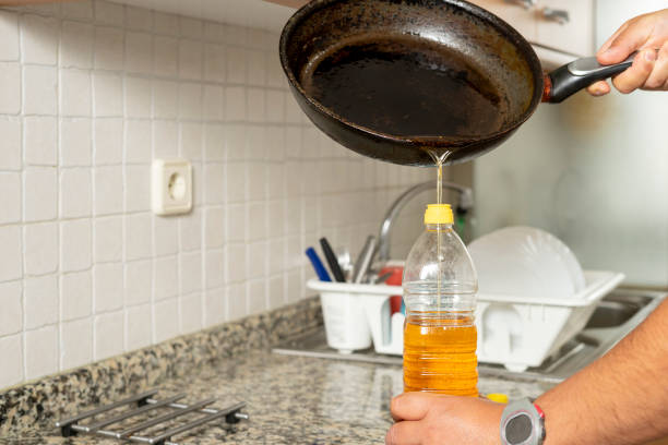 フライパンからリサイクルされた食用油を自宅のキッチンのペットボトルに入れる男。家庭でのリサイクルのコンセプト - 食用油 ストックフォトと画像
