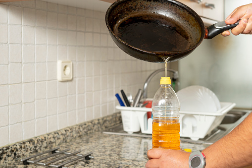 Man placing recycled edible oil from a frying pan into a plastic bottle in his home kitchen. Recycle at home concept