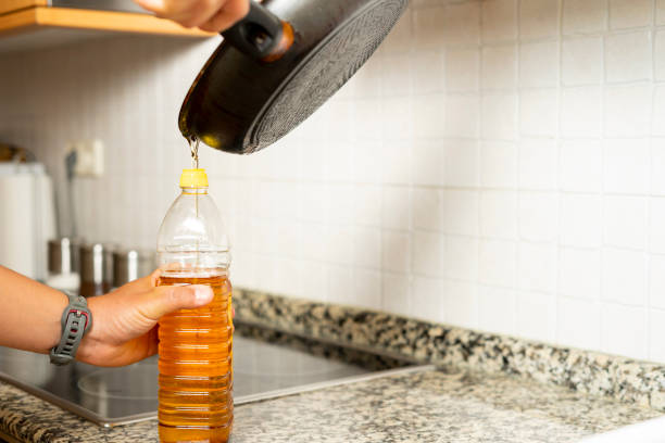 Close up of a man's hands recycling edible oil from a frying pan into a plastic bottle in his home kitchen stock photo