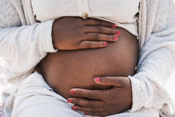 primer plano de una mujer embarazada africana sosteniendo su vientre - enfoque en las manos - embarazada fotografías e imágenes de stock