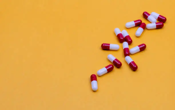 Top view of red-white capsule pills on yellow background. Pharmacy web banner. Pharmaceutical industry. Drug use in senior people concept. Health budget and life insurance topics background.
