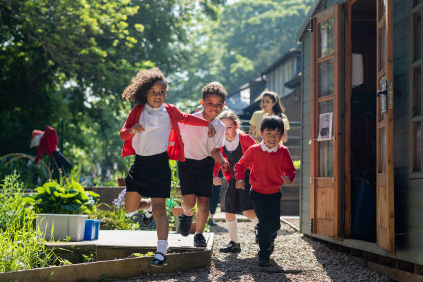 Running To Play A medium close-up of a group of school children running in the school yard as they head to playtime. Two of the children are siblings and go to the same school in Hexham in the North East of England. school uniform stock pictures, royalty-free photos & images