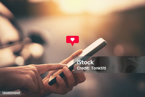 istock Close up woman hand hold using smart phone with heart icon at outdoor park street background. Copy space of technology business and travel holiday concept. 1340024049