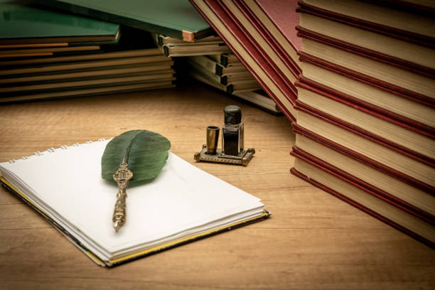 istock Old books stacked in disarray, an old pen with its ink and a notepad on an old wooden table and dim lighting. Selective focus. Vintage scene concept. Copy space. 1340025533