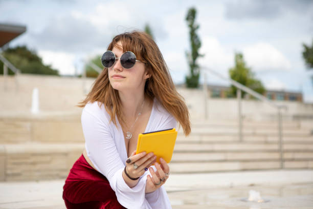 istock Young woman sitting on stone steps with an e-reader, outside in summer 1340027032
