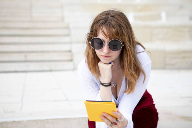 istock Young woman sitting on stone steps with an e-reader, outside in summer 1340027035