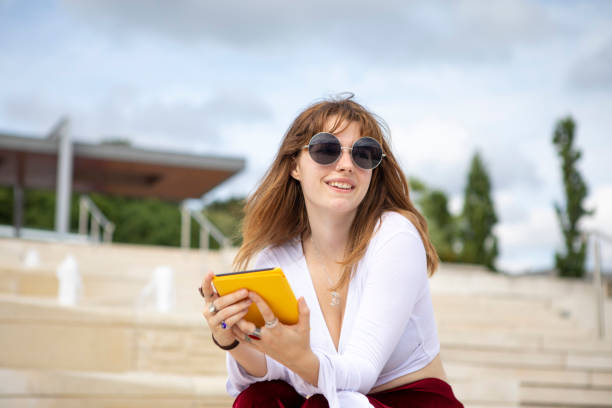 istock Young woman sitting on stone steps with an e-reader, outside in summer 1340027060