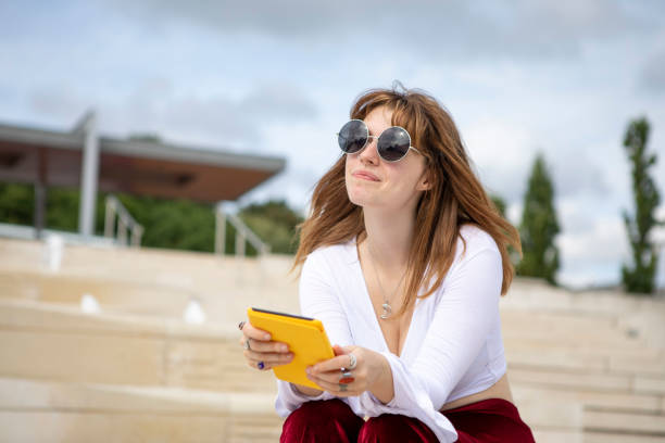 istock Young woman sitting on stone steps with an e-reader, outside in summer 1340027063