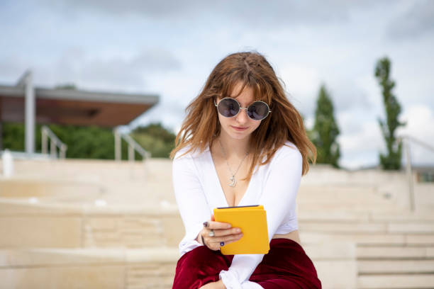 istock Young woman sitting on stone steps with an e-reader, outside in summer 1340027067