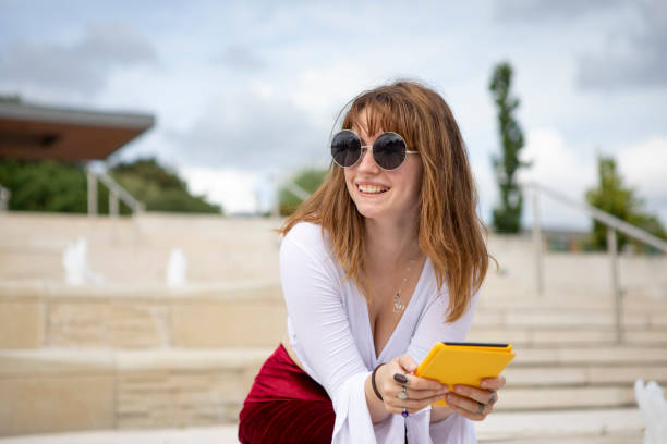 istock Young woman sitting on stone steps with an e-reader, outside in summer 1340027068