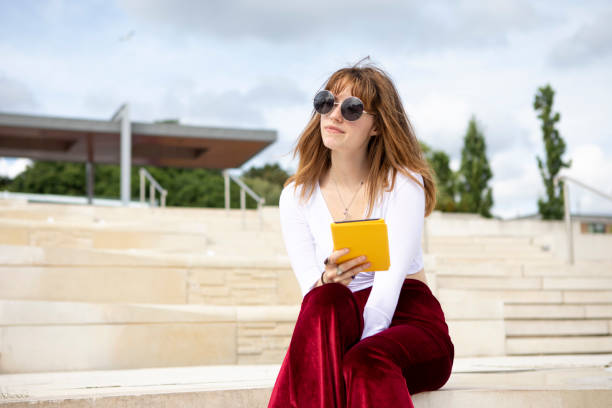 istock Young woman sitting on stone steps with an e-reader, outside in summer 1340027076