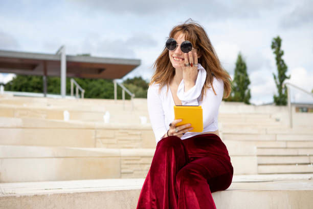 Young woman sitting on stone steps with an e-reader, outside in summer