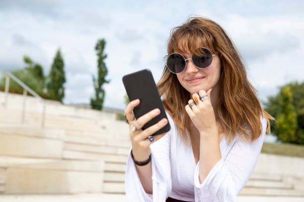istock Young woman sitting on stone steps using a mobile phone outside in summer 1340027125