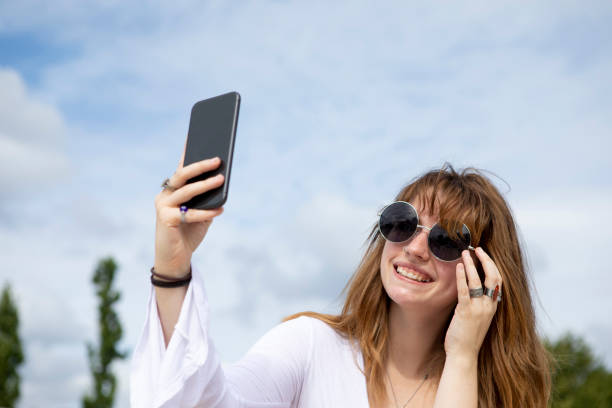 istock Young woman sitting on stone steps using a mobile phone to take a selfie outside in summer 1340027143