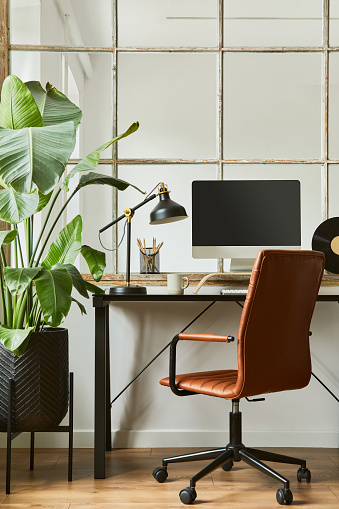 Creative composition of modern masculine home office workspace interior with black industrial desk, brown leather armchair, pc and stylish personal accessories. Template.