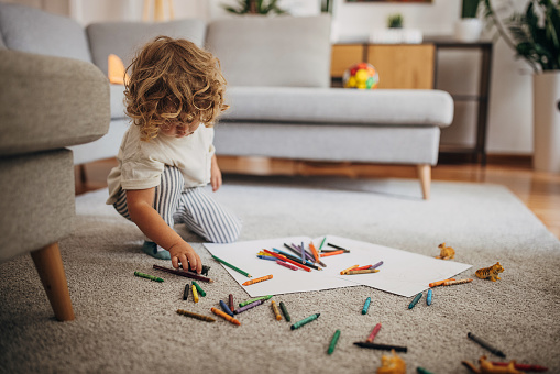 Little boy drawing and coloring in the living room on the floor