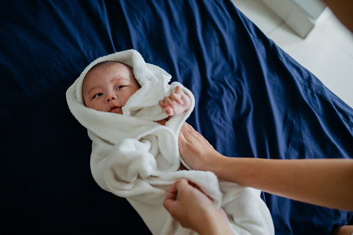 Image of an Asian Chinese woman wrapping and drying her baby boy with towel on bed after bath