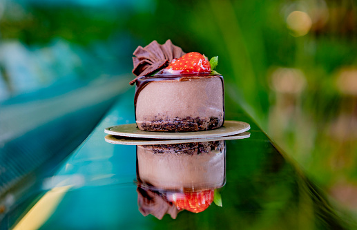 Closeup of individual Chocolate mousse with chocolate chip base and dark chocolate ganache with candied strawberry topping on a green nature background and on a gold reflective surface in Sri Lanka