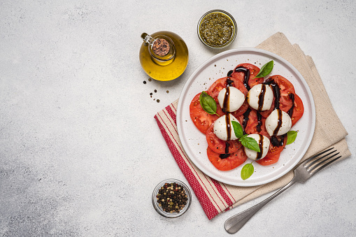 Caprese salad with tomatoes, basil, mozzarella, balsamic sauce and olive oil. Traditional Italian food. Top view, white background, copy space