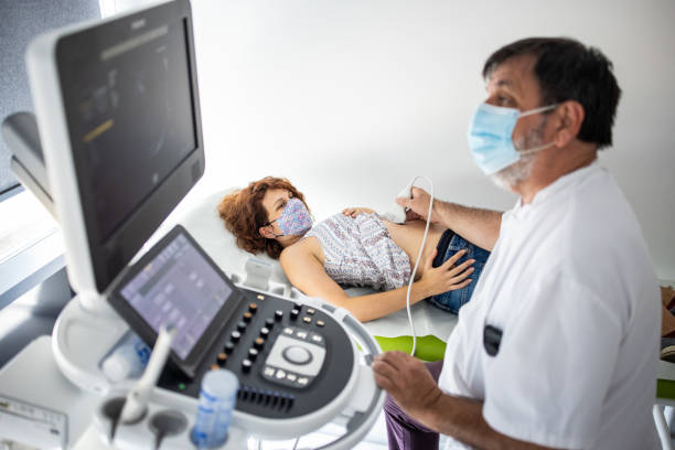 jeune femme enceinte avec masque facial protecteur subissant un examen échographique dans une clinique médicale - human pregnancy ultrasound medical exam doctor photos et images de collection