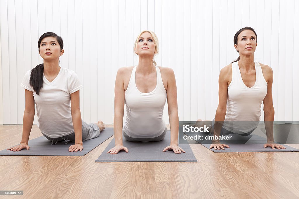 Interracial Group of Three Beautiful Women In Yoga Position An interracial group of three beautiful young women stretching in a yoga position at a gym Active Lifestyle Stock Photo