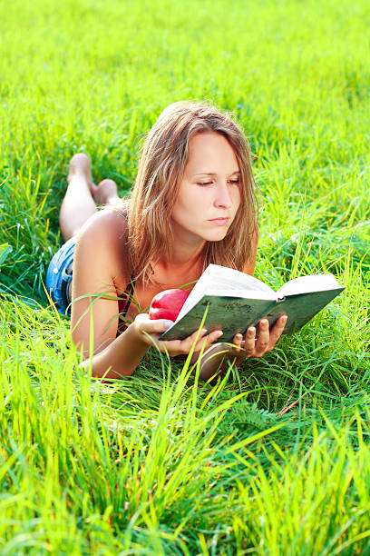 istock Young woman lying in grass reading book 134004364