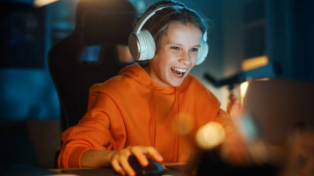 excited young boy in headphones playing video games on laptop computer in cozy dark room at home. happy successful teenager beating players and winning at the online competition. - smiling research science and technology clothing imagens e fotografias de stock