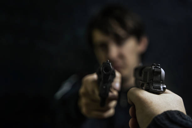 istock Man's hand with pistol pointed at criminal with revolver. 1340046583