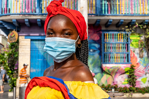 Cartagena de Indias, Colombia - May 22, 2021: Colombian woman with facial mask in Cartagena de Indias with the traditional dress during Covid-19 pandemic . In Colombia is usual to transport fresh fruit on the head.