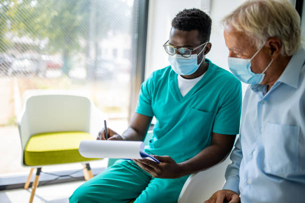 enfermera masculina que tiene una conversación con un paciente mayor en la clínica médica - pollution mask fotografías e imágenes de stock