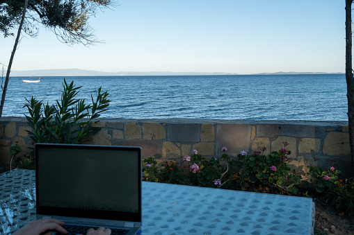 Woman working seaside on laptop and drink coffee, remote professional work life in holiday, home office
