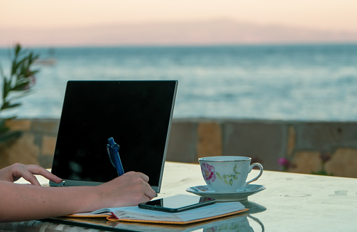 Woman working home writing and taking notes at the beach, writing on the notebook for work, remote job mobile in pandemic