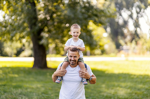 Freedom in nature, a family weekend in the park. A father carries his son on his shoulders. Parenting and happy childhood. Father and son spend funny time in nature on a sunny summer day
