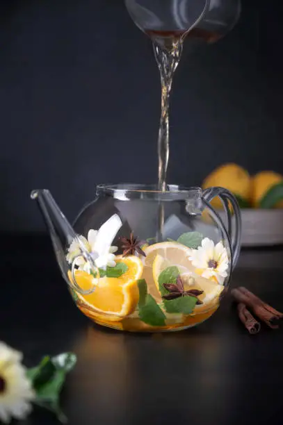 Glass teapot with fruit citrus tea on black background. Herbal calendula healthy drink