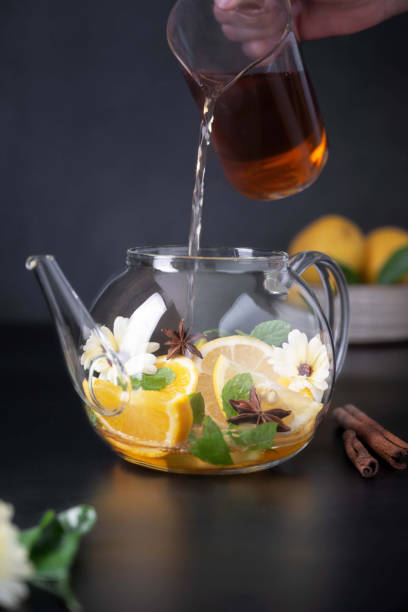 istock Fruit citrus tea and glass teapot on black background. Herbal calendula healthy tea 1340066344