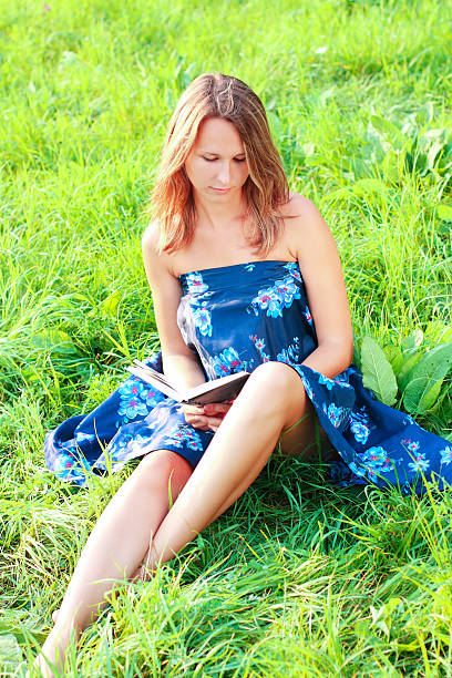 istock Young woman sitting in grass reading book 134006889