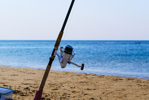 Fishing rod with spinning reel on beach. Saltwater fishing on sea shore. Copy space.