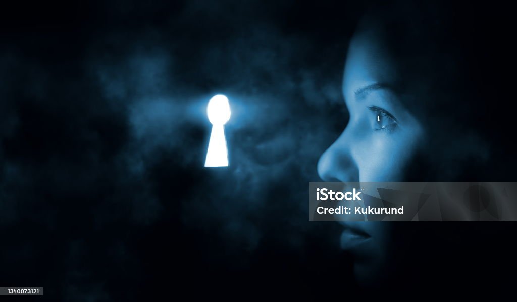 the woman's face in the dark looks through the keyhole glowing blue mysterious light Keyhole Stock Photo