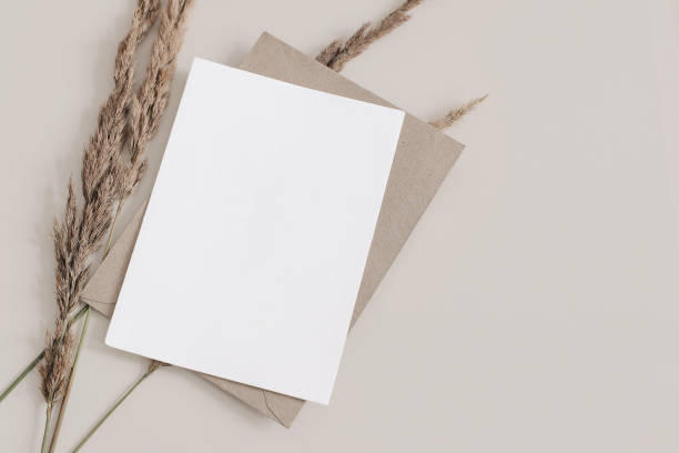 istock Fall wedding, birthday stationery composition. Blank greeting card, invitation mockup with brown envelope. Dry grass, festuca plant on Beige table background. Autumn flat lay, top view. Copyspace 1340075051