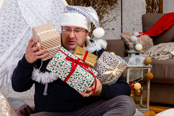 istock middle-aged man with glasses and a silver dwarf hat with Christmas gift boxes in a decorated room 1340075741