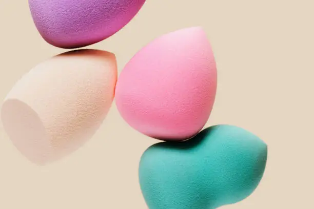 Colored cosmetic beauty blender sponges on nude colored background with copy space. Green, violet, pink, rainbow colored sponges different shape.