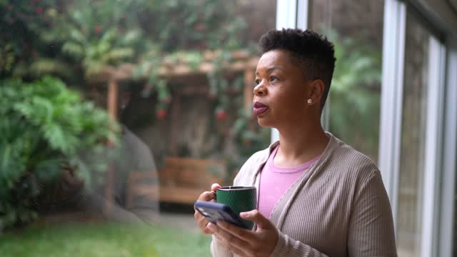 Happy woman using smartphone and contemplating at home