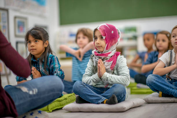 Preschool children practicing mindfulness in a classroom A multi ethnic group of preschool children are seated on the classroom floor. They each have a meditation mat that they are sitting on. They have the palm of their hands together as they are practicing meditation with their teacher who is sitting in front of them. afghan hound stock pictures, royalty-free photos & images