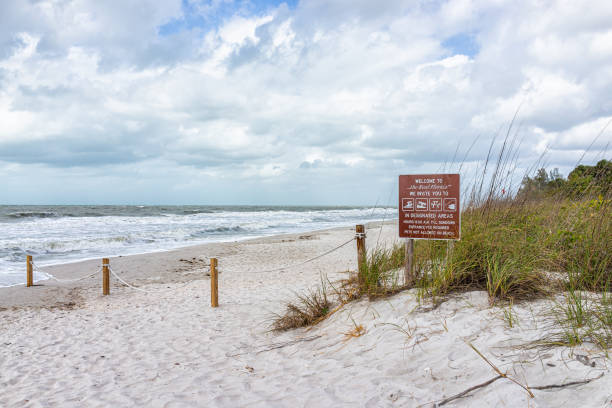 vanderbilt beach in florida city by sand dunes and sea oats with dramatic ocean gulf of mexico landscape, rope fence and sign for swimming, fishing boating and picnic - florida weather urban scene dramatic sky imagens e fotografias de stock
