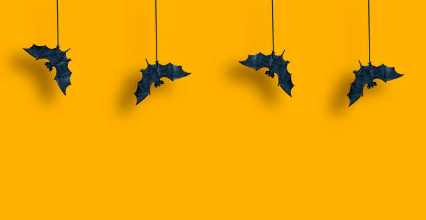 Horizontal pattern. Black bats in row are suspended with spread wings on yellow orange background. Hallowen. Copy space