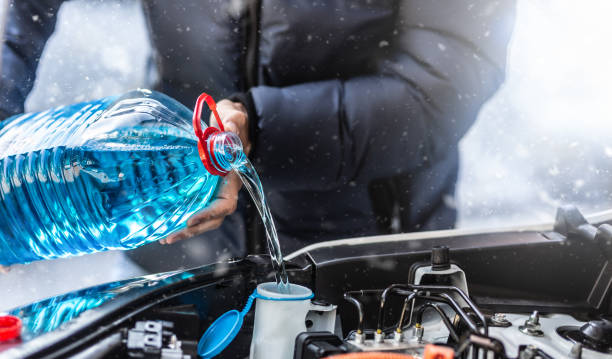kierowca wlewa płyn niezamarzający do zbiornika, aby spryskać przednią szybę podczas burzy śnieżnej. - auto repair shop adult auto mechanic blue zdjęcia i obrazy z banku zdjęć