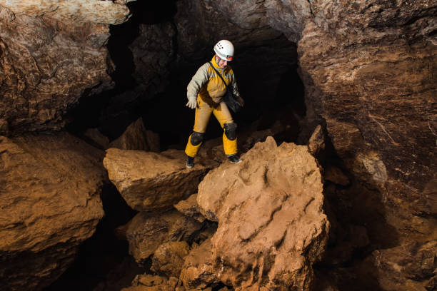 Tourist in a protective suit and helmet with a flashlight explores the cave. Extreme active sport
