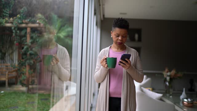 Woman using smartphone and contemplating at home