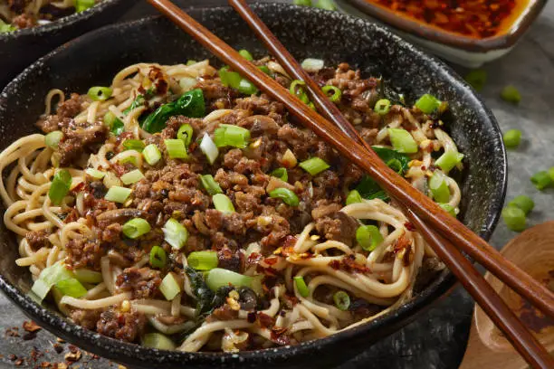 Dan Dan noodles, a Pork dish originating from Chinese Sichuan cuisine. with a spicy sauce containing, chili oil, crispy fried minced pork, mushrooms, bok choy and scallions served over noodles.