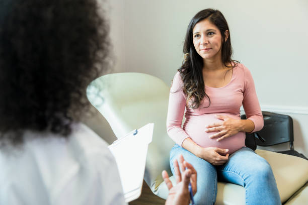 Expectant mother touches abdomen while listening to unrecognizable doctor stock photo